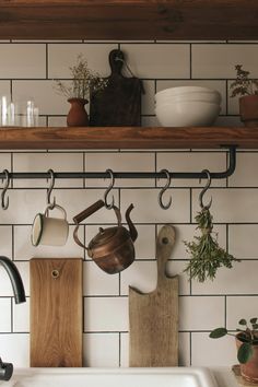 pots and pans are hanging on the wall above a kitchen sink with wooden cutting boards