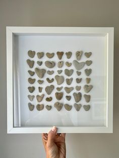 a person holding up a framed photo with rocks in the shape of hearts on it