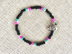 Stackable, coastal, beachy, boho, artsy love bead, stretchy bracelet, one size ~7-7.25 inches fits most womens' wrists. Bold design of black, pink and turquoise features prominent metal turtle bead, symbol of longevity and sustainable ocean life. Pairs well with other marine designs. Black Bead Bracelet, Metal Turtle, Stackable Beaded Bracelets, Overhand Knot, Beachy Boho, Glass Seed Beads, Bold Design