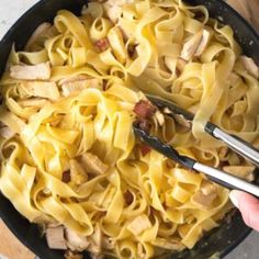 someone is holding tongs over some noodles in a skillet with meat and cheese