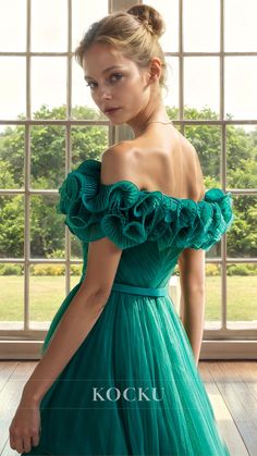 a woman in a green dress is standing by a window