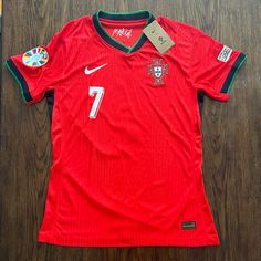 a red soccer jersey with the number seven on it sitting on a wooden floor next to a bottle opener