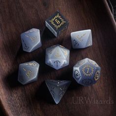 six dice with gold designs on them sitting on a wooden table next to another dice