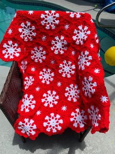 a red and white crocheted blanket sitting on top of a chair next to a swimming pool