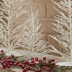 two white christmas trees sitting on top of a wooden table next to red berries and pine cones