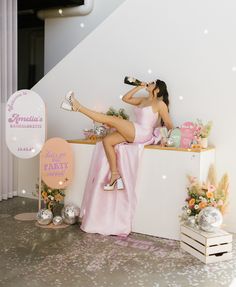 a woman sitting on top of a counter drinking from a wine bottle while wearing high heels