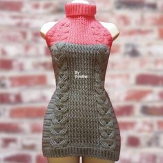 a mannequin with a knitted dress on display in front of a brick wall