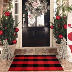 two potted christmas trees on the front porch with ornaments hanging from it's sides