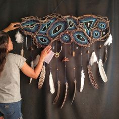 a woman is working on an art piece with feathers hanging from the wall behind her