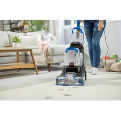 a woman is vacuuming the carpet with a blue and white cordless mop