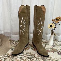 a pair of cowboy boots sitting on top of a rug next to a vase with flowers