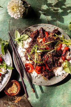 two plates filled with rice and meat on top of a green table next to flowers