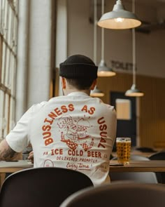 a man sitting at a table with a beer in front of him and looking out the window