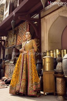 a woman standing in front of some vases wearing a yellow and red outfit with gold accents