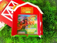 an open book on top of some green grass next to a red and white barn