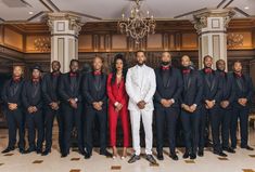 a man and woman standing in front of a group of men wearing tuxedos