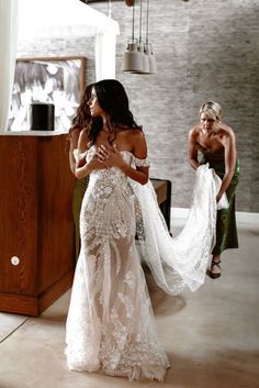 two women in wedding dresses standing next to each other and one is holding her dress