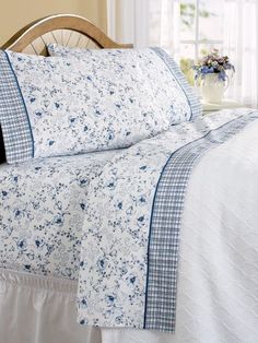 a bed with blue and white floral bedspread on top of it next to a window