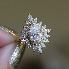 a woman's hand holding a ring with a large diamond in the middle and small diamonds around it