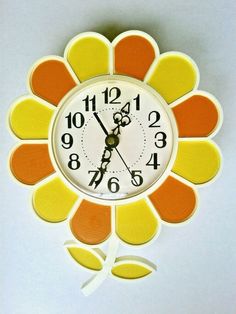 an orange and yellow flower shaped clock hanging from the side of a wall with numbers on it