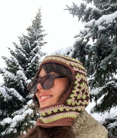 a woman wearing sunglasses and a knitted hat standing in front of snow covered trees