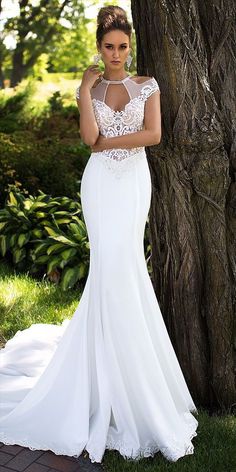 a woman standing next to a tree wearing a white dress with sheer neckline and open back