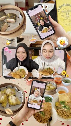 two women holding up their cell phones while sitting at a table full of food