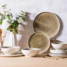 a table topped with plates and bowls next to a vase filled with flowers on top of a wooden table