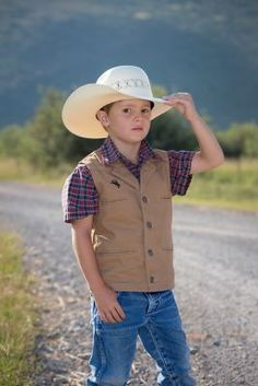 The Youth Bronco Canvas Vest is made from our premium 12 ounce cotton canvas, is durable and strong, just what the upcoming little working rancher and cowboys need. This vest has several unique elements, one being the shoulder western yoke on the front and back of the vest, an open v-neck with lapel and four Wyoming Traders logo buttons. This vest is lined with a polyester satin lining. The Bronco Vest has four front welt pockets, two for your hands and two chest pockets, all lined with a polyes Western Rodeo Vest, Western Style Sleeveless Vest For Rodeo, Athena Lee, Canvas Vest, Brown Vest, Cream Shirt, Tractor Supply, Kids Outerwear, Polyester Satin