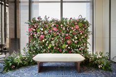 a white bench sitting in front of a window covered in pink and green flowers next to a plant wall