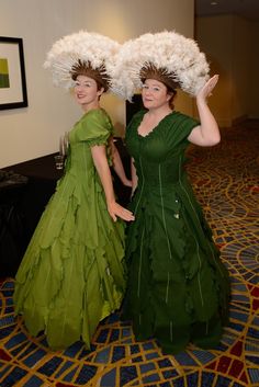 two women dressed in green dresses with large white flowers on their heads, standing next to each other