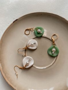 two white and green heart shaped earrings on a plate with gold earwires hanging from them