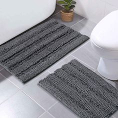 two bathroom rugs on the floor in front of a bathtub and toilet with a potted plant