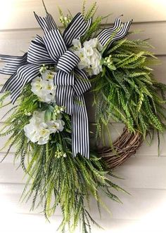 a wreath with white flowers and greenery hanging on a door hanger that is decorated with black and white striped ribbon