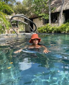 a woman wearing a red hat floating in a pool with clear blue water and palm trees