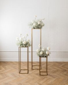 two gold plant stands with white flowers in them