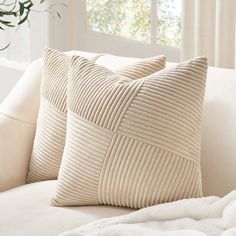 a white couch with two pillows sitting on it's side and a plant in the background