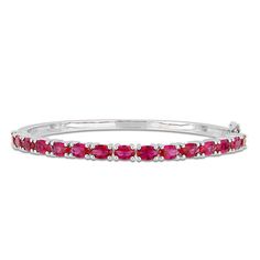 Polish off any attire with this simply stunning bangle bracelet. Crafted in sterling silver, this beautiful style showcases a row of 6.0 x 4.0mm oval-shaped lab-created bright red rubies. Buffed to a brilliant luster, this bracelet measures 7.0 inches in circumference and secures with a tongue and groove clasp. Ruby Bangles, Bangle Design, Classic Bangles, Ruby Bracelet, Gemstone Bangle, Sterling Silver Bangle Bracelets, Peoples Jewellers, Tongue And Groove, Silver Bangle Bracelets