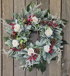 a wreath with white roses, greenery and pine cones on a wooden fence background