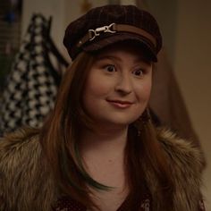 a woman with long hair wearing a brown hat and fur collared jacket, smiling at the camera