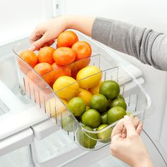 two people reaching into an open refrigerator with fruit in it