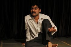 a man sitting on the floor in front of a black curtain with his hands out