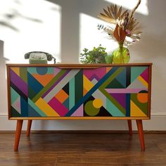 a colorful painted cabinet sitting on top of a hard wood floor next to a wall