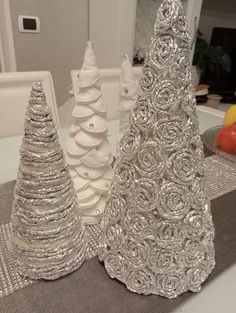 three silver christmas trees sitting on top of a table next to an apple and orange