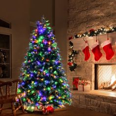 a brightly lit christmas tree sitting in front of a fire place with stockings on it