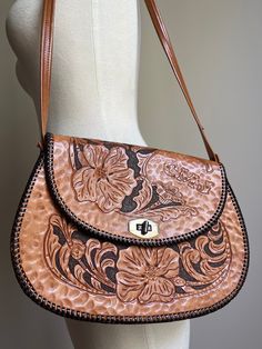 Vintage 70s hand tooled shoulder bag. Beautiful floral design. Stitched accents. Gold tone hardware. Substantial weight to this leather piece. Inside features dark brown leather lining. Three compartments total with one open pocket, one zippered and the main interior space. Additional measurement and condition information provided for your consideration. Maker: - Initialed CMJ on top flap. RAU hardware. Era: 1970s Material: Estimated to be genuine leather Lined: Yes - estimated to be leather Condition: Bag is in Very Good Vintage Condition (scale: Mint, Excellent, Very Good, Good, Fair, Poor.) The straps show normal wear and a few stitches and seams have un-raveled at the center of the strap - see photo. Tooled art remains intact and in good condition.  WIDTH: 10 3/4 inches at widest point Vintage Brown Hobo Bag With Adjustable Strap, Retro Hand-tooled Bags, Brown Saddle Shoulder Bag With Removable Pouch, Vintage Brown Hand Tooled Bag For Travel, Vintage Brown Hand-tooled Travel Shoulder Bag, Hand Tooled Vintage Brown Travel Shoulder Bag, Vintage Brown Hobo Bag With Leather Backing, Vintage Brown Hand Tooled Bag For Everyday Use, Brown Hand Tooled Shoulder Bag For Everyday Use