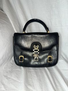 "Gorgeous vintage handbag that is in need of a little TLC, circa probably 1970s. Front closure has three toggle \"lengths\" and there are two faux buckle details. The exterior leather could use a shining up, but otherwise is in pretty good condition. The interior, sadly, has quite a bit of pen marking inside, but is in functionally great shape. Interior zip pocket still opens smoothly and is clean - please see photographs for item you will receive. For high quality vintage fashion at an affordab Vintage Satchel With Metal Hardware, Retro Satchel With Metal Hardware, Retro Satchel Bag With Metal Hardware, Vintage Shoulder Bag With Metal Hardware, Retro Satchel With Gold-tone Hardware For Daily Use, Retro Travel Satchel With Brass Hardware, Vintage Formal Satchel With Metal Hardware, Vintage Satchel With Metal Hardware For Travel, Vintage Crossbody Bag With Gold-tone Hardware