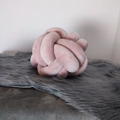 a large pink pillow sitting on top of a fur covered tablecloth next to a white wall