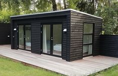 a small black cabin with sliding glass doors and wooden decking in the middle of a grassy area