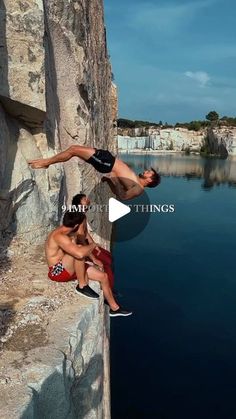 two men hanging out on the side of a cliff next to a body of water